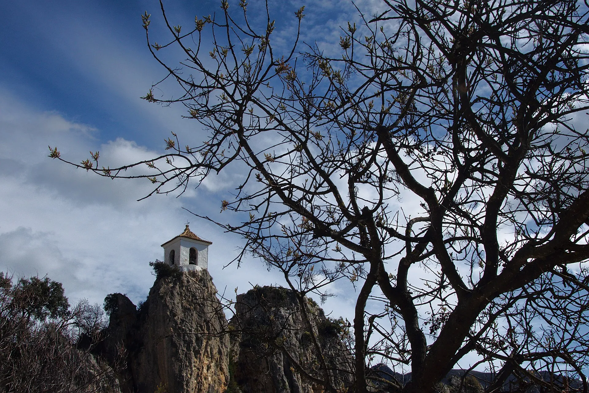 Vista de un pueblo blanco de montaña con iglesia rodeado de paisaje verde mediterráneo